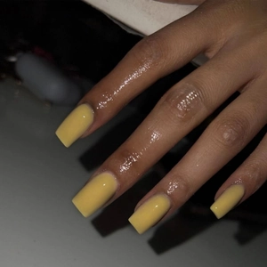 Detail of glossy yellow square press-on nails on fingers with a radiant shiny finish
