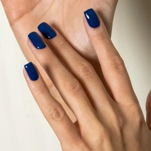 Close-up of glossy deep blue square-oval press-on nails on model's hand with shiny finish