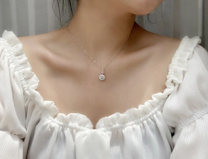 Macro shot of S925 silver clover necklace with round clear crystal on model's neck
