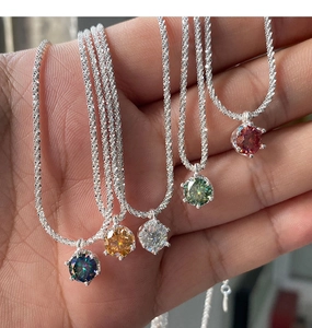 Close-up of five colorful six-prong moissanite crown pendants on silver wavy chains