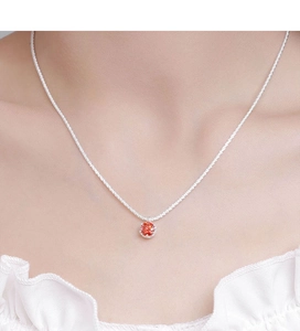 Close-up of a silver crown-set necklace featuring a sparkling orange-red moissanite stone
