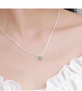 Close-up of a sparkling green moissanite crown pendant on a delicate silver chain