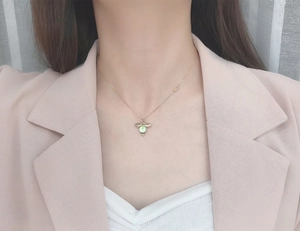 Close-up of golden bee pendant with green moonstone worn by a model in a pink suit