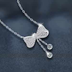 Moissanite bow necklace with tassel pendants in 925 silver on textured blue background