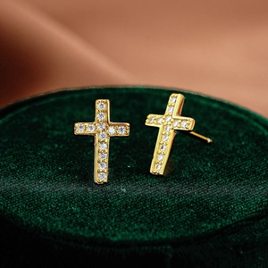 Elegant gold cross earrings with sparkling moissanite stones on green velvet