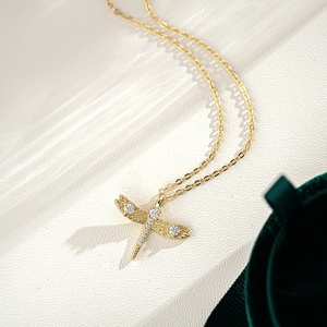 Détail du pendentif libellule en or avec moissanite sur fond de cuir blanc élégant
