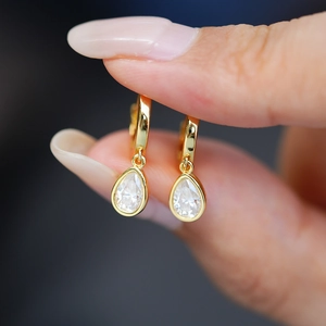 Close-up of teardrop moissanite earrings with 14K gold plated base held in fingers