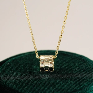 Gros plan du pendentif cylindrique doré à motif alvéolé serti de moissanites étincelantes