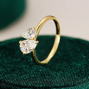Macro view of gold Toi et Moi ring with dual pear cut moissanite stones on green velvet