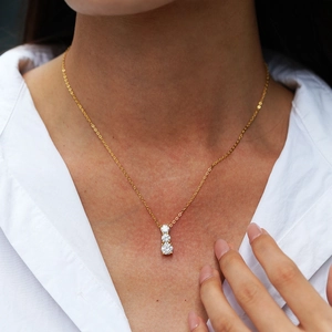 Three-stone Moissanite pendant necklace in gold finish worn on a white shirt