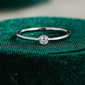 Close-up of a S925 sterling silver ring with a bezel-set moissanite on green velvet