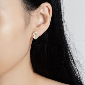 Elegant gold dollar sign stud earrings with pavé crystals shown on model's ear