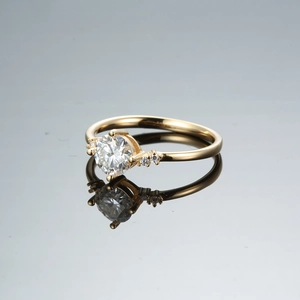 Detail of champagne gold moissanite ring with six-prong setting on reflective surface