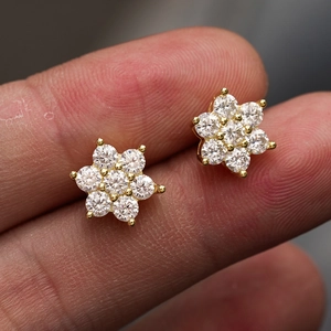 Macro view of gold flower earrings with round-cut moissanite stones held by hand