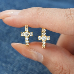 Gros plan de boucles d'oreilles croix en or avec moissanite sur fond en denim bleu