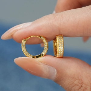 Handansicht goldener Creolen mit mikroverpflastertem Moissanit auf Denim-Hintergrund