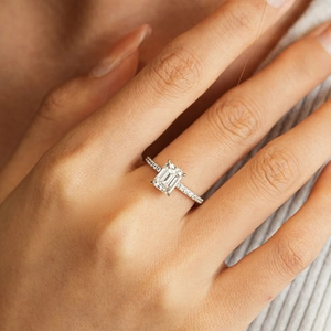 Elegant emerald cut moissanite ring with pave-set band on a female model hand