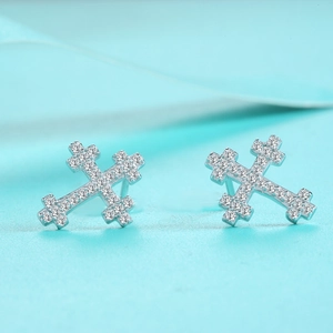 Macro shot of silver cross earrings with full pave moissanite on blue background