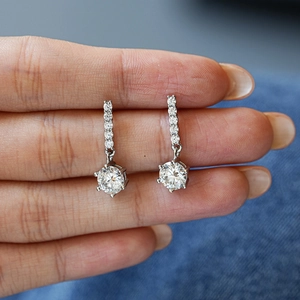 Elegant s925 silver six-prong moissanite earrings held by hand on denim background