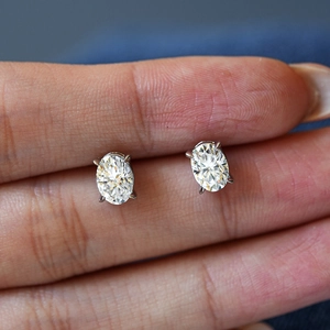 Oval cut moissanite stud earrings in four-claw S925 silver setting shown held by hand