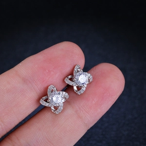 Macro shot of silver four-leaf clover moissanite stud earrings held by fingers