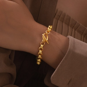 Detail of a golden round bead chain bracelet featuring a classic toggle clasp on a model