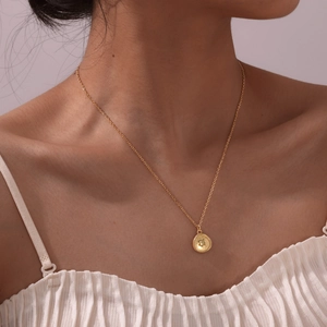 Detail of 18K gold-plated necklace with a textured coin pendant and animal relief on model