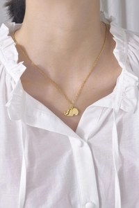 Close-up of a gold elephant pendant necklace worn by a model on a white shirt