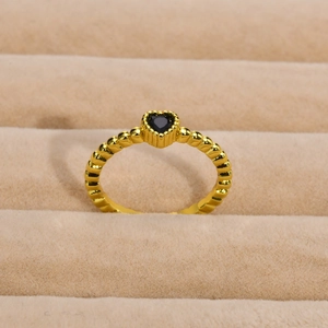 Dettaglio macro di un anello a sfere dorato con uno zircone nero a forma di cuore