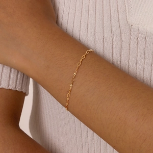 Détail d'un bracelet minimaliste à chaîne en losange doré porté sur le poignet