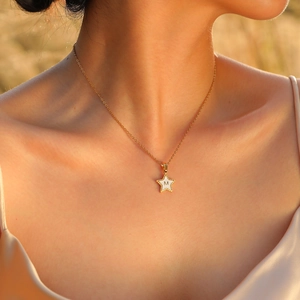 Close-up of a gold star pendant necklace with white enamel and letter M on a model