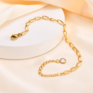 Detail of a gold stainless steel chain bracelet with a clear zircon pendant on a white stand