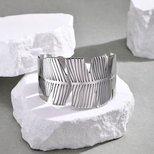 Dettaglio macro del bracciale rigido in acciaio argento con motivi floreali e piume