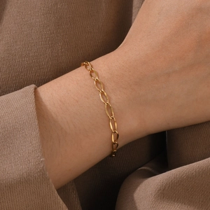 Detailed view of an 18K gold minimalist chain bracelet worn on a wrist over soft knitwear
