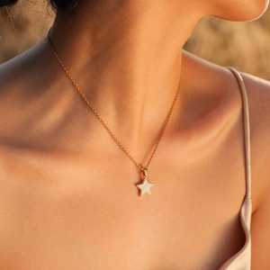 Gold star necklace with initial M pendant worn by a model in warm elegant lighting