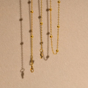 Minimalist gold-plated bead chain with lobster clasp hanging over a matte surface