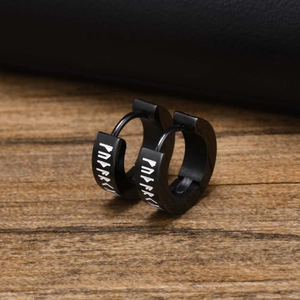 Detailed view of black stainless steel earrings with white Viking Rune patterns on wood