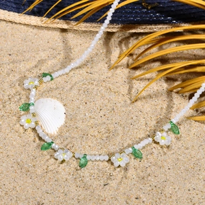 Détail d'un collier de perles style plage avec breloques marguerites sur un fond de sable