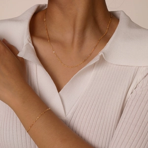 Ensemble collier et bracelet minimaliste en acier inoxydable doré porté sur polo en tricot