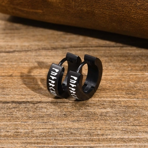 Close-up of black stainless steel viking rune earrings on a rustic wood surface