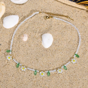 Collier en acier inoxydable avec marguerites blanches et feuilles vertes sur fond de sable