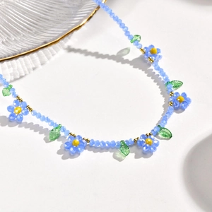 Détail d'un collier de perles bleues fait main avec fleurs marguerites et perles dorées