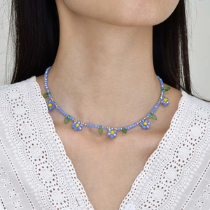 Détail du collier de perles marguerite avec pétales bleus et accents de feuilles