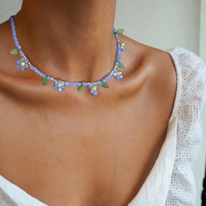 Détail du collier de perles marguerite bleue avec pendentifs feuilles sur le décolleté