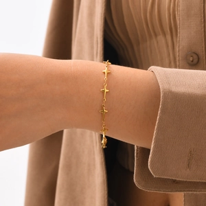Détail d'un bracelet doré avec des étoiles à quatre branches porté au poignet au style épuré