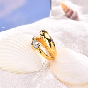 Gold stainless steel oval zircon ring set displayed on white sand with sea shells
