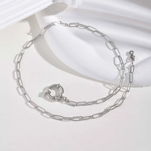 Silver paperclip link necklace with a round decorative spring clasp on a stone surface