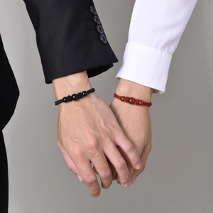 Detail of woven heart magnetic couple bracelets in red and black on intertwined hands