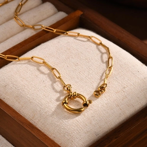 Detail of 18K gold stainless steel paperclip chain with decorative sailor clasp on linen