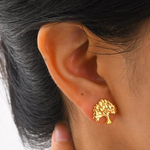 Close-up of golden Tree of Life stud earrings on a female ear with detailed engraving